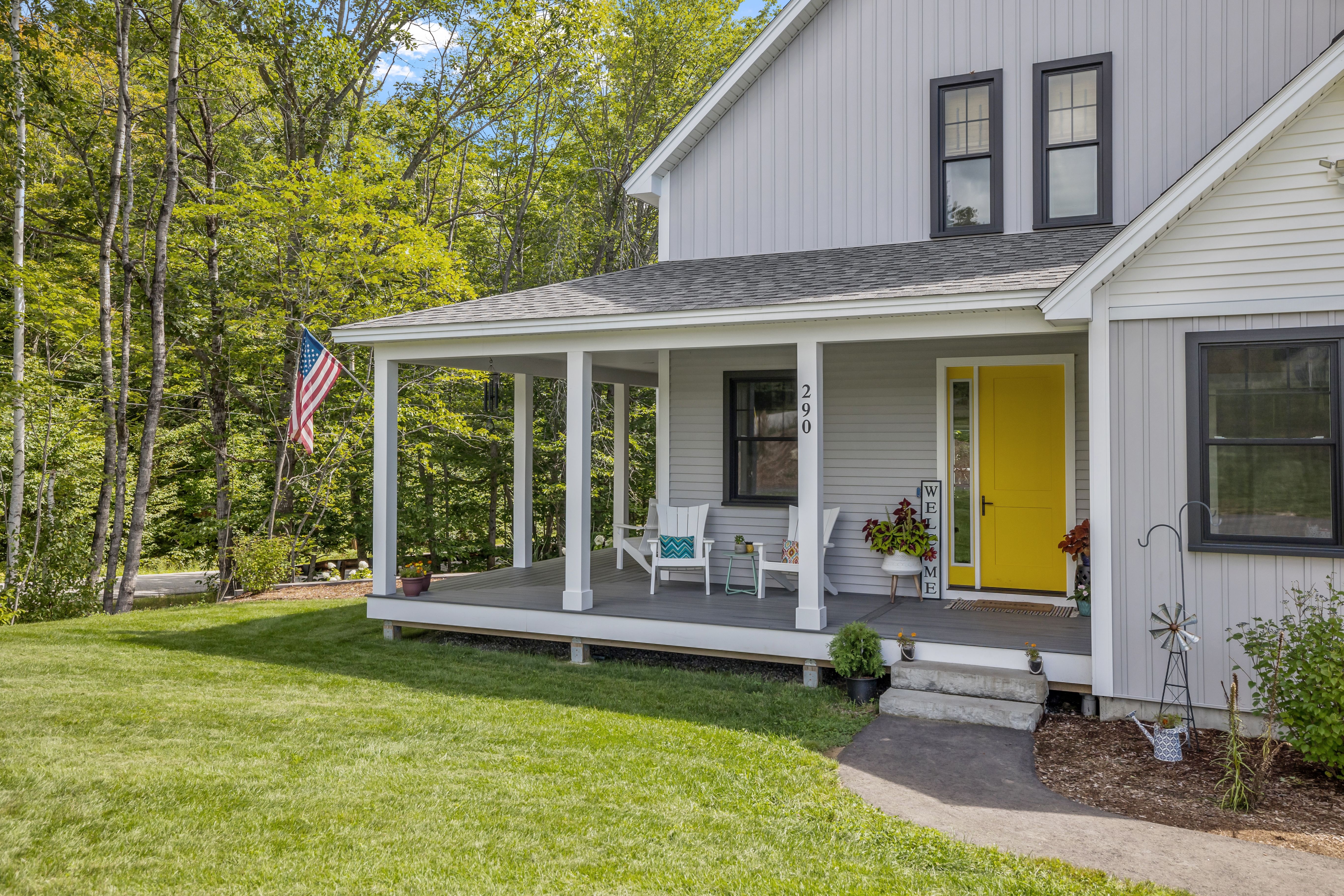 An image of a New England style home that recently used a HELOC to improve their property value. On the porch there is a welcome sign, two chairs, and flowers. The door to the home is a bright yellow.