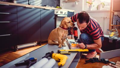 A man doing home renovations in the kitchen while his dog watches. There are power tools all around the floor. He used a HELOC to finance these home improvements.