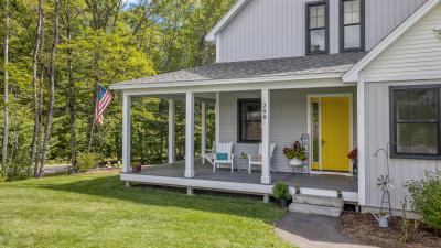 An image of a New England style home that recently used a HELOC to improve their property value. On the porch there is a welcome sign, two chairs, and flowers. The door to the home is a bright yellow.